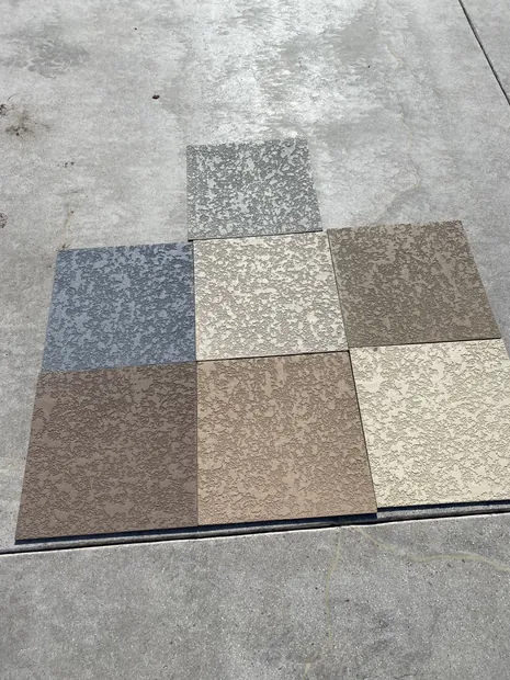 Six textured deck coating sample squares in grays, tans and cream laid out on a concrete slab