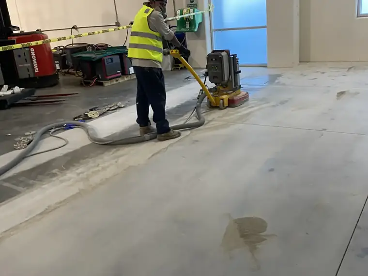 Worker in a high-visibility vest running a grinder across an interior concrete floor