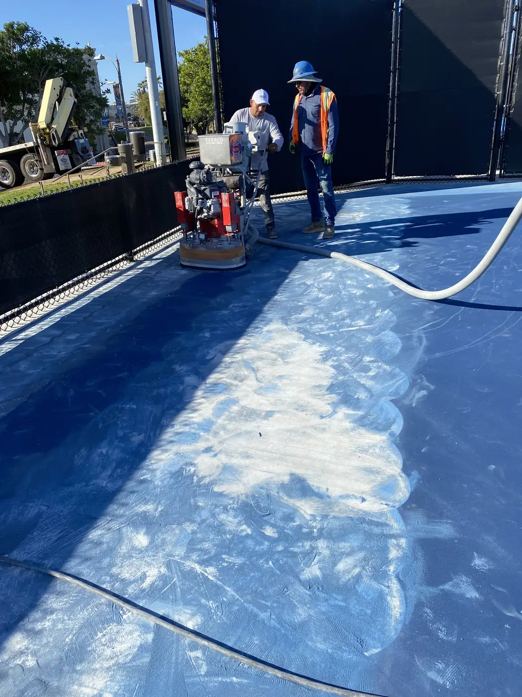 Crew grinding the blue surface off a pickleball court in bright sun