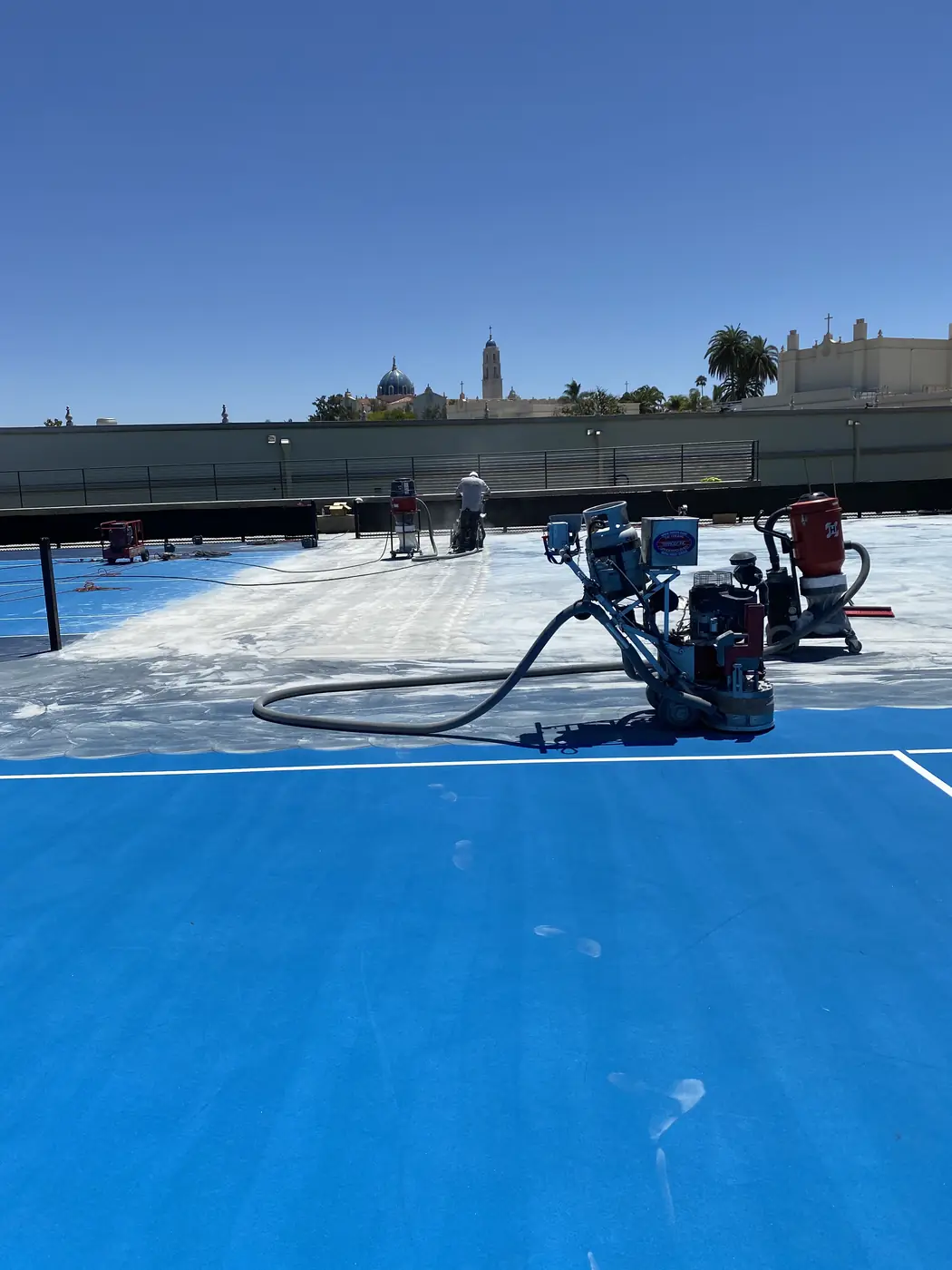 Grinder stripping the blue coating from a court, bare concrete showing behind