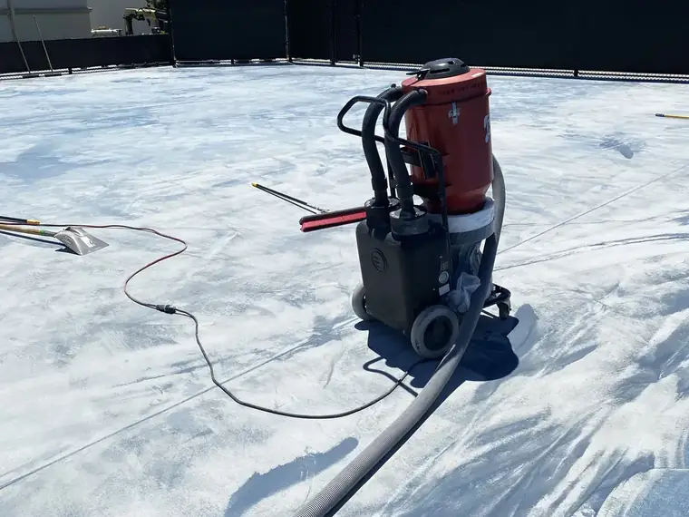 Walk-behind grinder and hose on a court stripped back to gray concrete