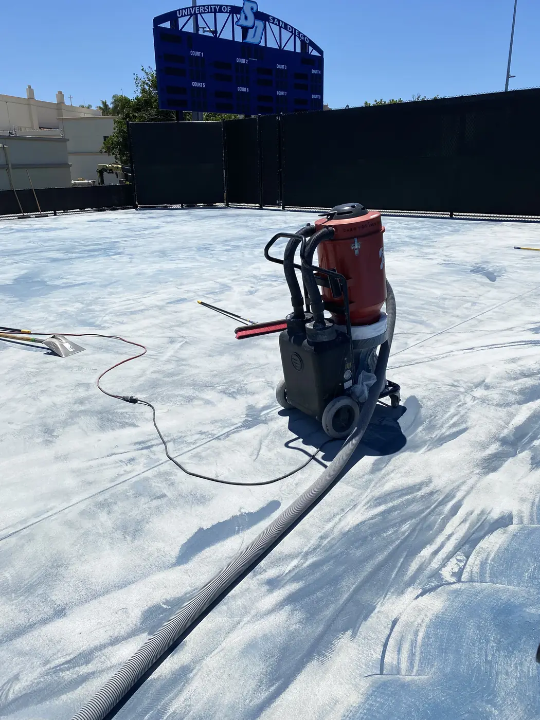 Walk-behind grinder and hose on a court stripped back to gray concrete