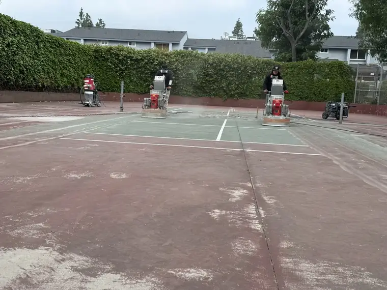 Green painted tennis court with white lines and grinding machines set up along the baseline