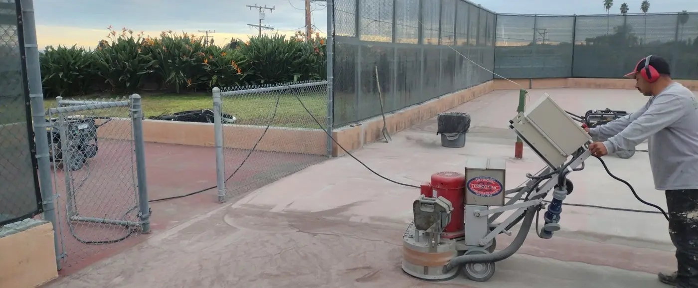 Grinding equipment on a court beside a chain link fence and lawn