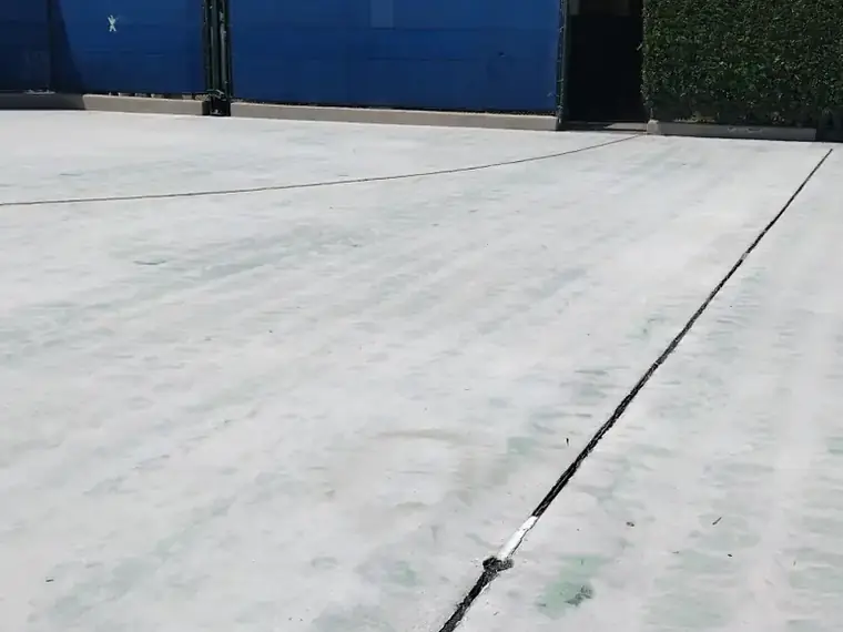 Court surface ground back to clean gray concrete against a blue wall