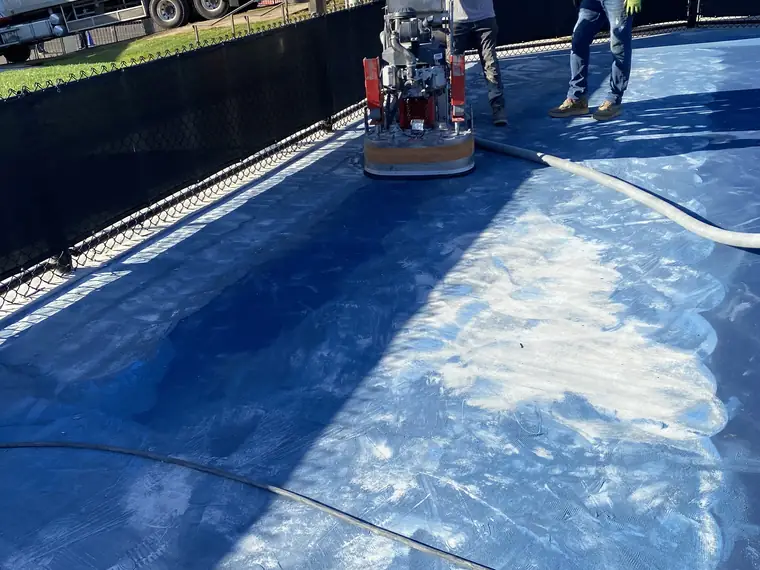 Grinder cutting a pale stripe through the blue coating on a sports court