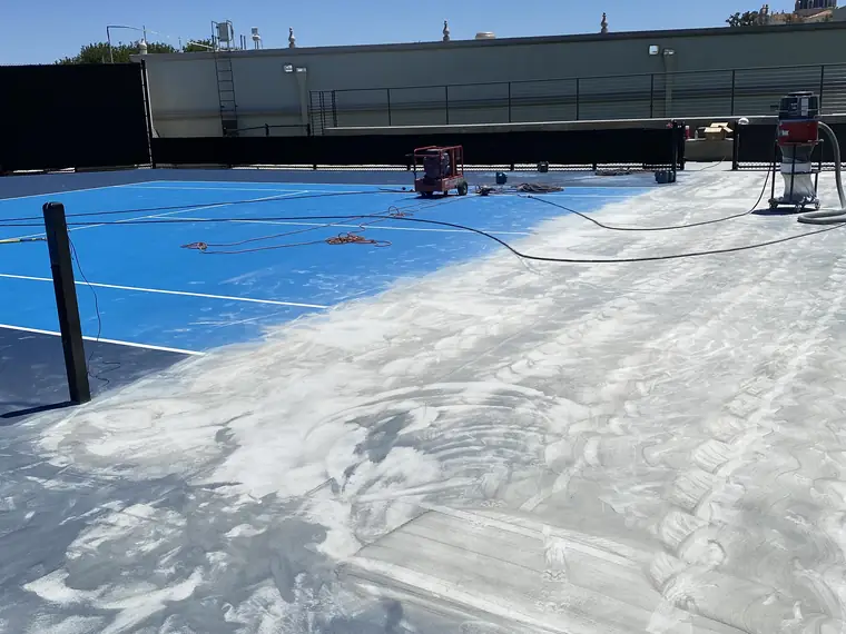 Blue sports court with a wide band of coating already ground away