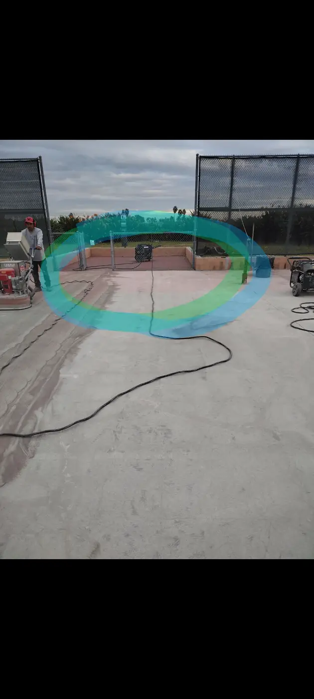 Crew grinding a pool deck with the old teal and green coating still visible
