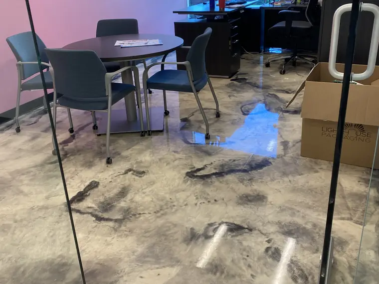 Metallic epoxy floor reflecting the ceiling lights beside a glass meeting room