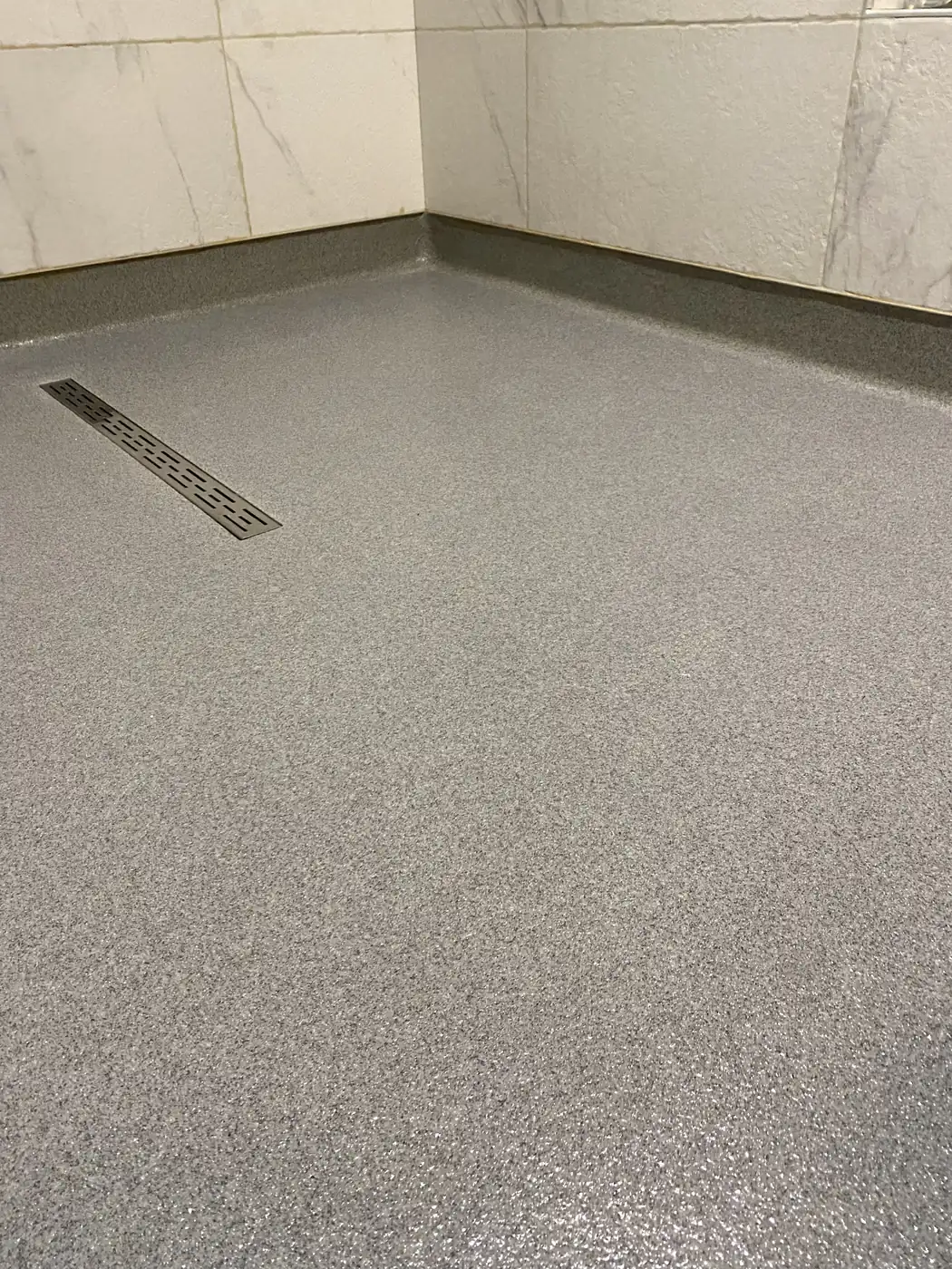Gray flake epoxy floor with a stainless trench drain and coved wall base