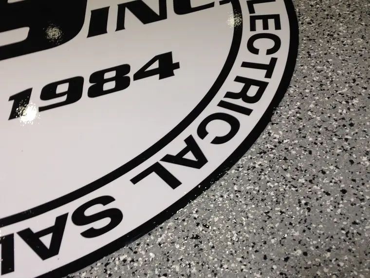 Close view of an electrical company logo inlaid into a gray flake epoxy floor