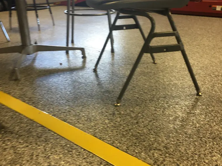 Olive flake epoxy shop floor with a yellow boundary line and a work chair