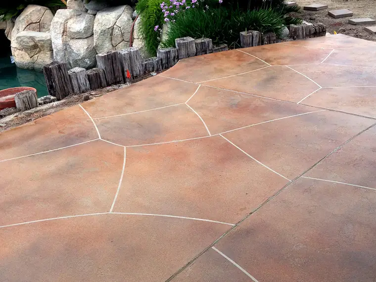 Terracotta stained patio cut in a flagstone pattern beside tropical planting