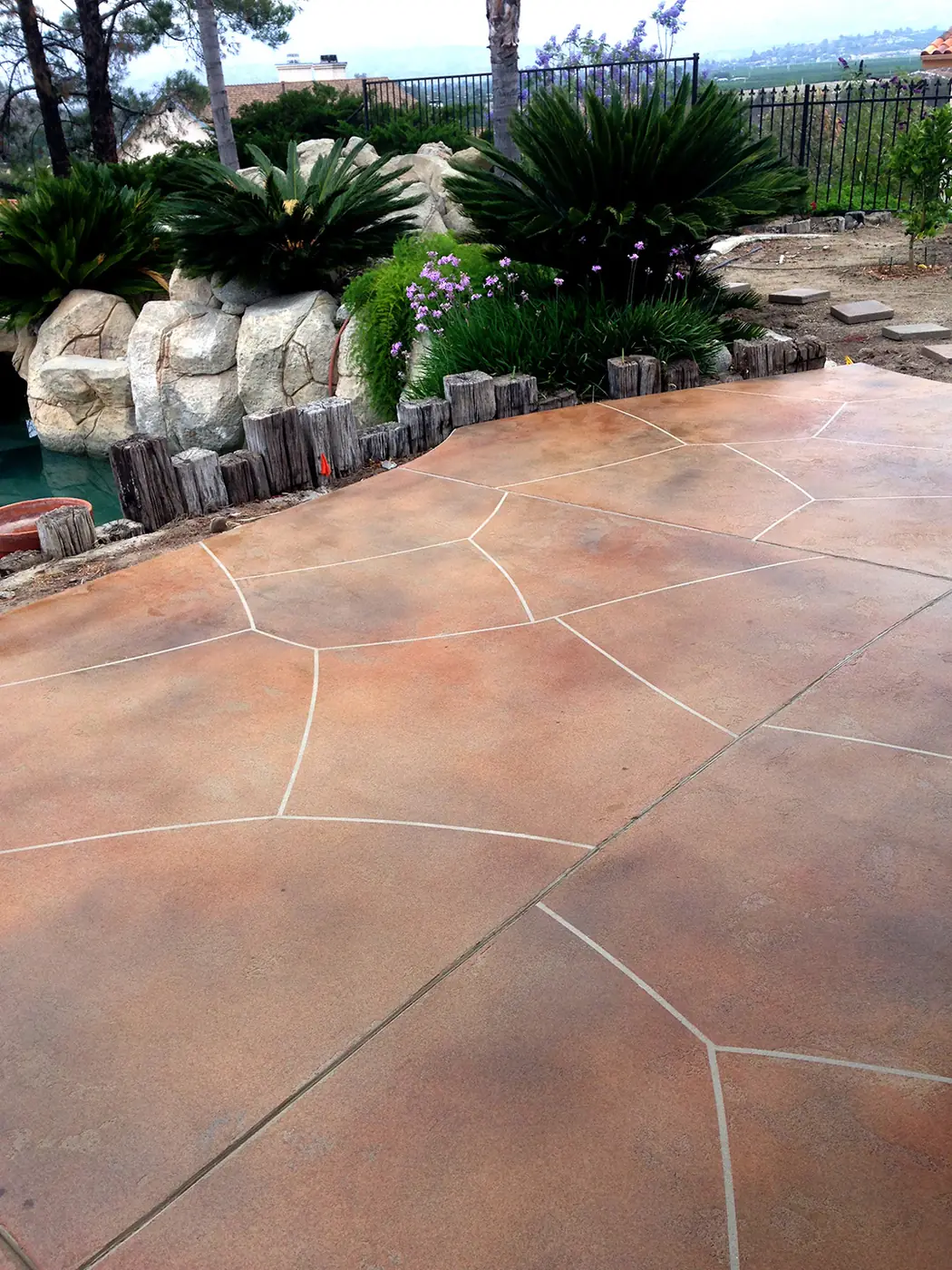 Terracotta stained patio cut in a flagstone pattern beside tropical planting