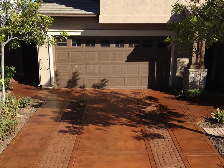 Rust stained driveway with a brick border in front of a two-story home