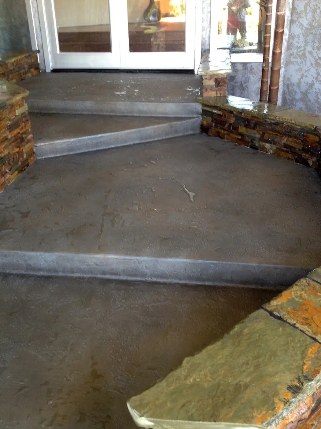 Gray and brown stained entry steps beside a stone-faced planter