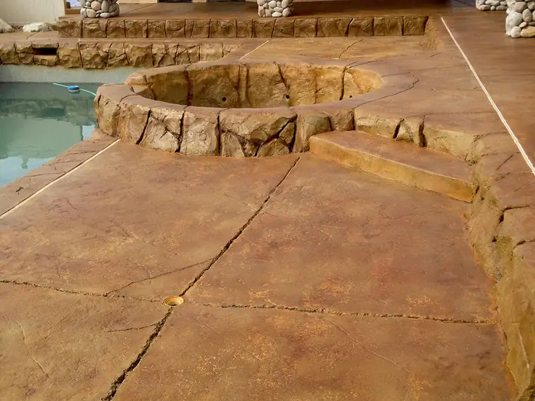 Gold and orange stained pool deck with a raised rock feature