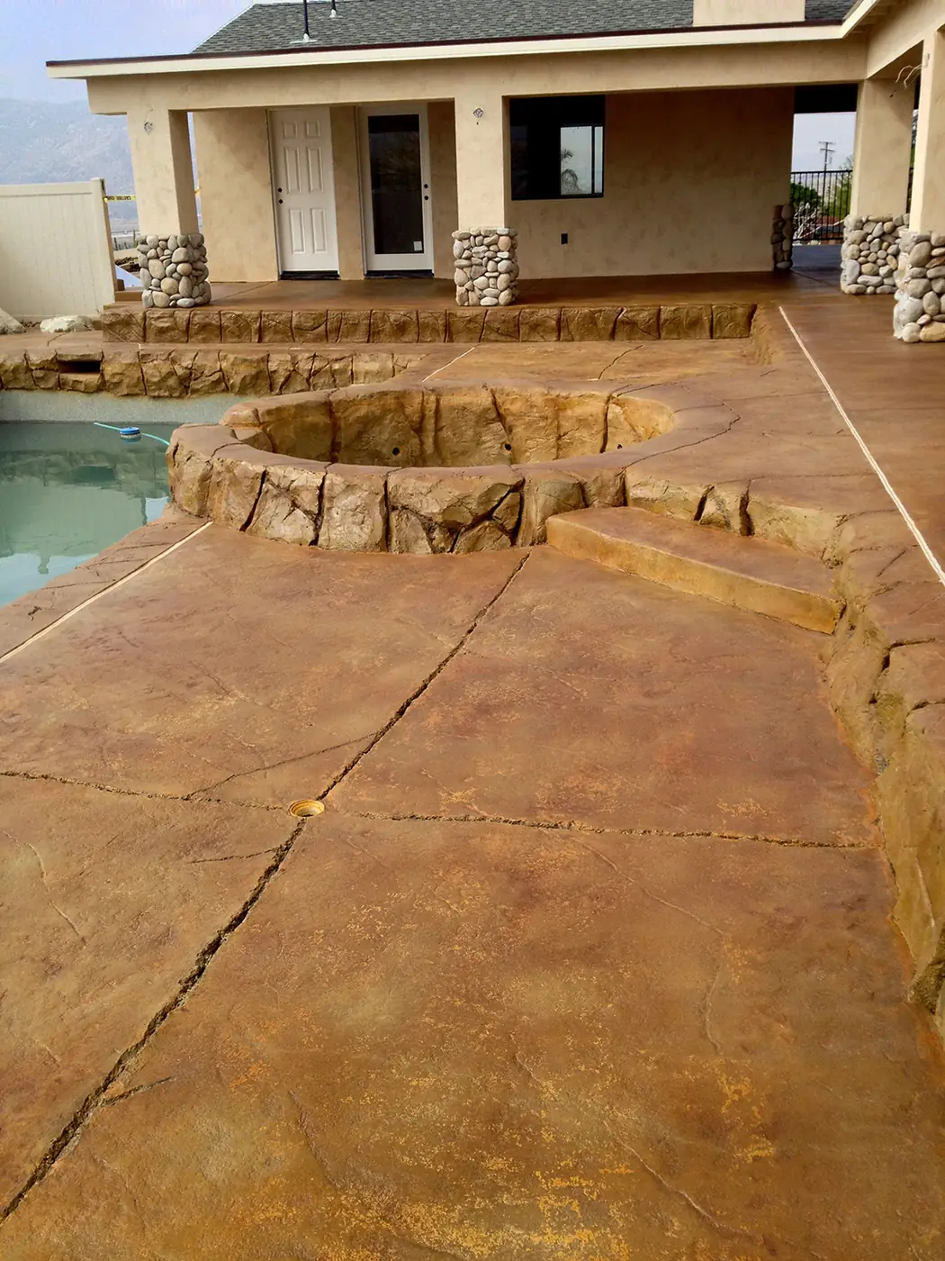 Gold and orange stained pool deck with a raised rock feature