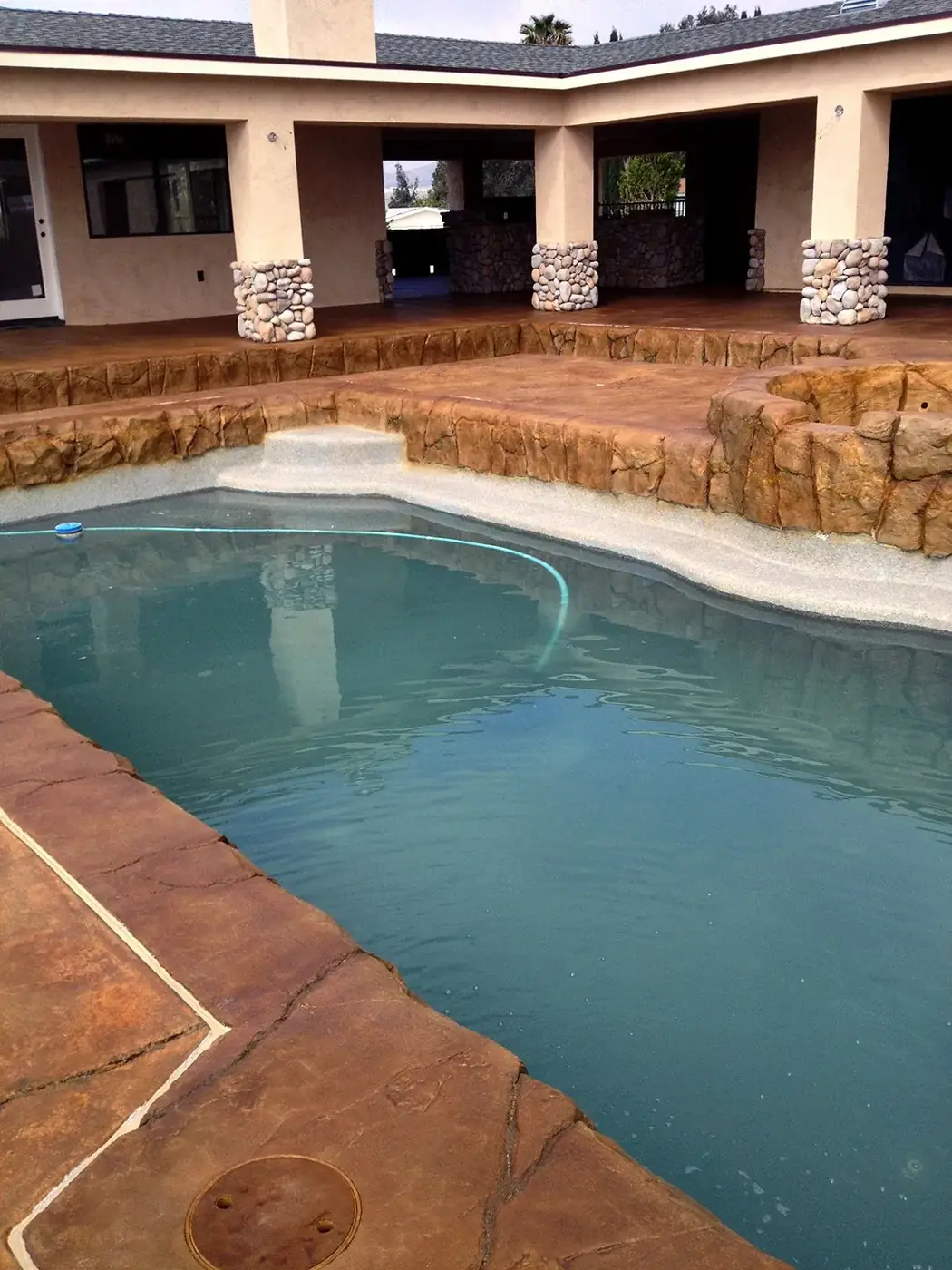 Stained pool deck in warm brown with a raised spa and rock feature