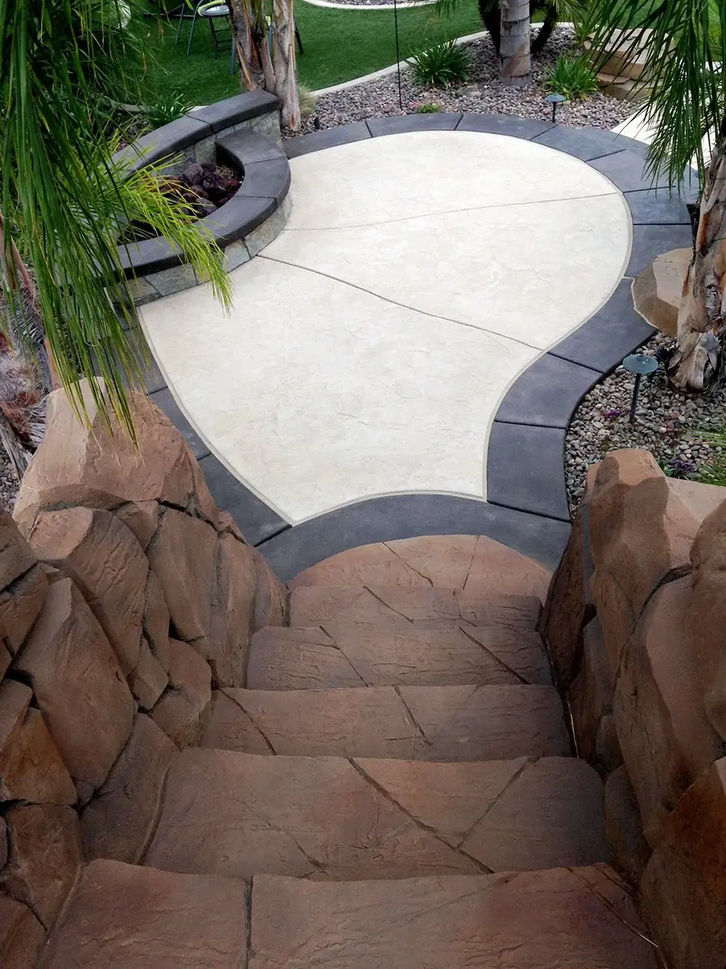 Cream and gray stained deck curving between rock features and a pool