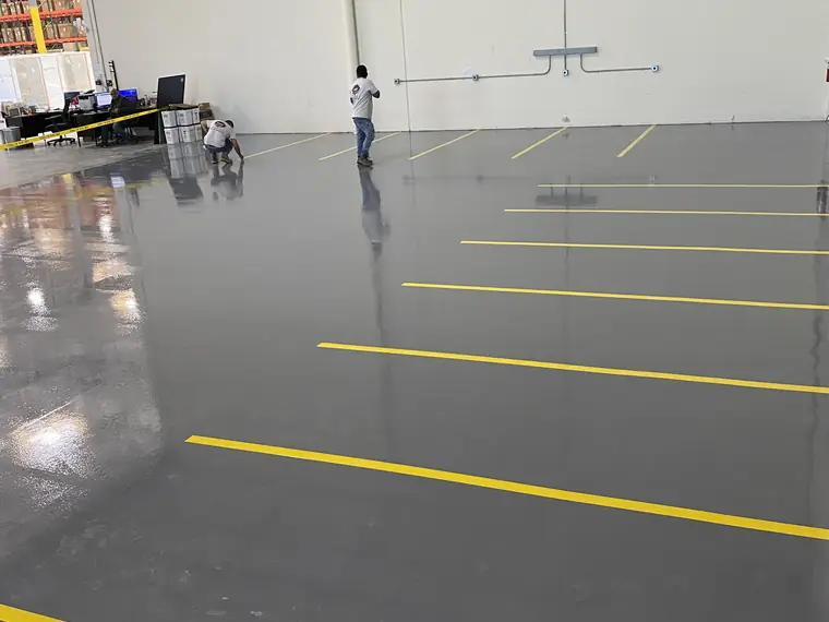 Gray epoxy warehouse floor marked out with yellow aisle striping while crews work at the far wall