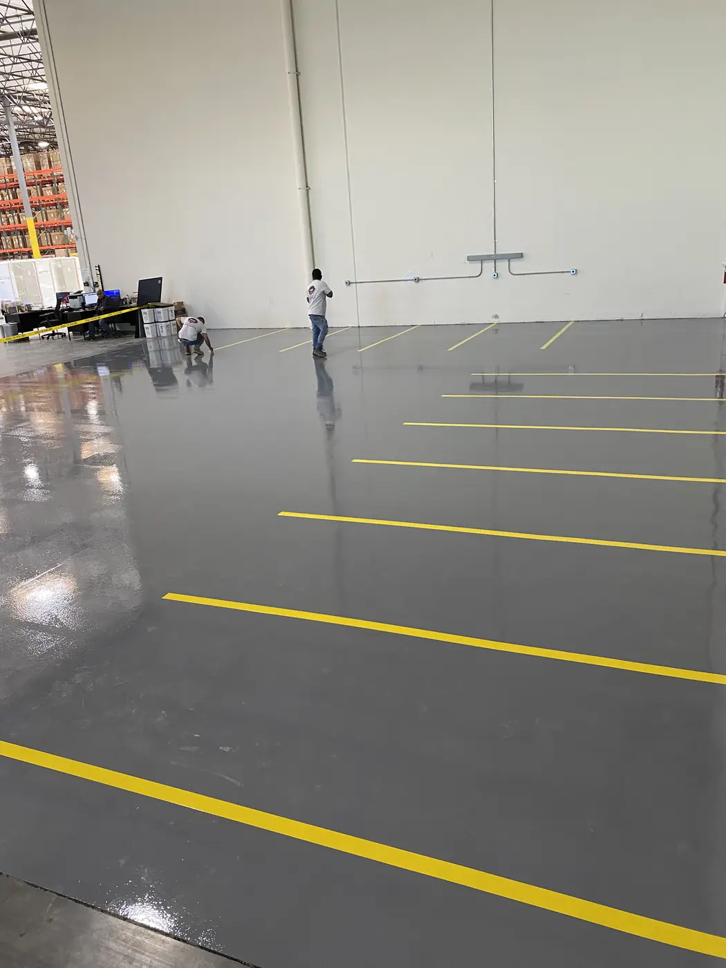 Gray epoxy warehouse floor marked out with yellow aisle striping while crews work at the far wall