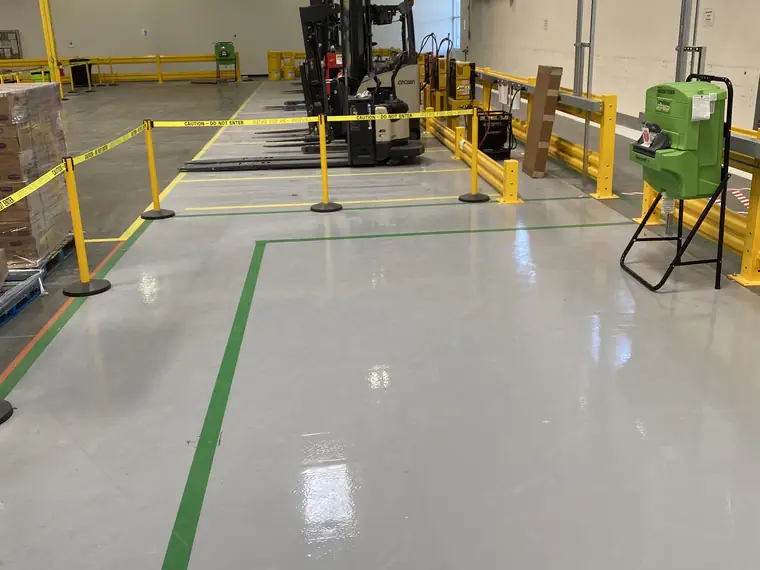 Warehouse floor in gray epoxy with green walkway striping, yellow guard rails and a forklift