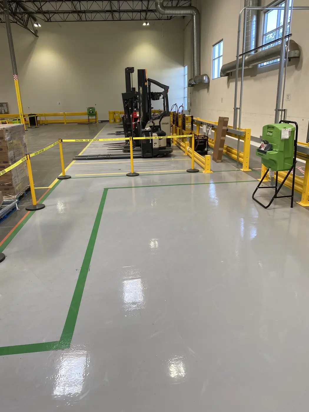 Warehouse floor in gray epoxy with green walkway striping, yellow guard rails and a forklift