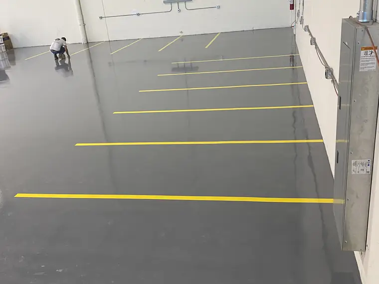 Gray epoxy warehouse floor with yellow aisle lines and a worker at the far end
