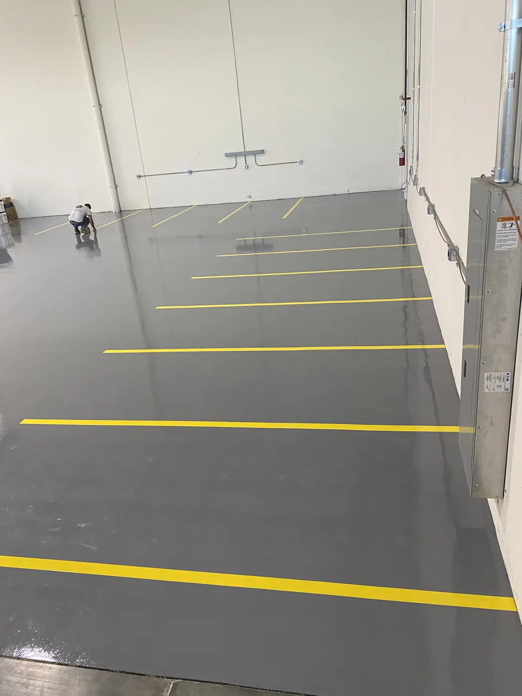Gray epoxy warehouse floor with yellow aisle lines and a worker at the far end