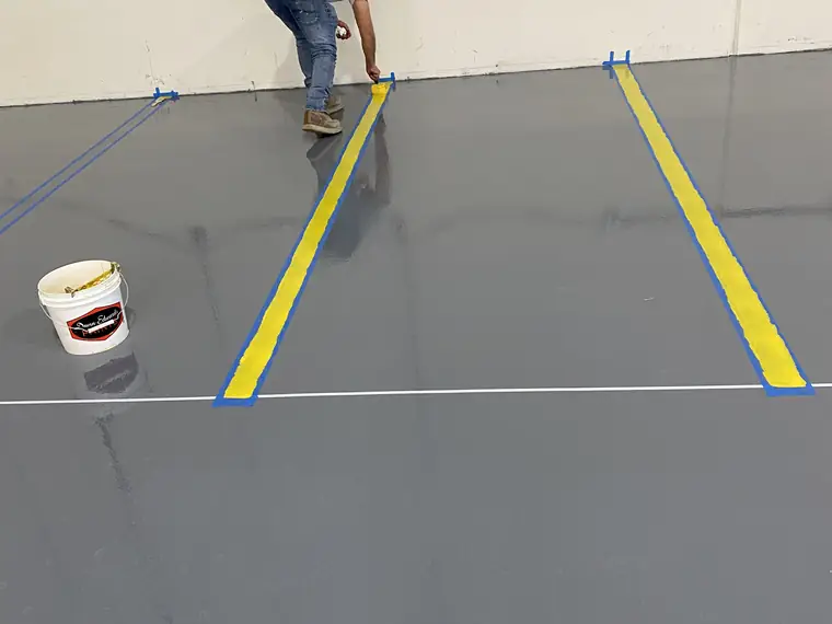 Worker taping out a yellow safety line on a freshly coated gray epoxy floor
