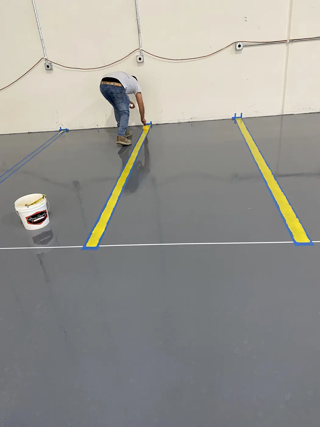 Worker taping out a yellow safety line on a freshly coated gray epoxy floor