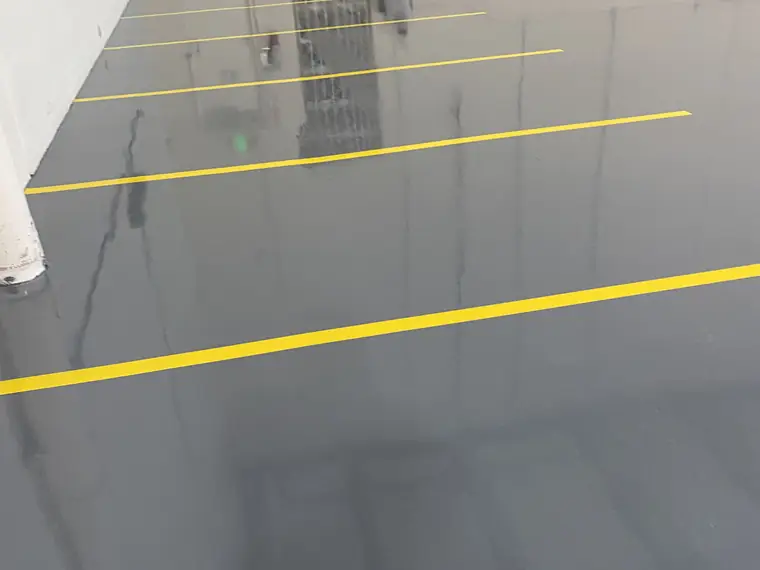 Gray epoxy warehouse floor with yellow striping and a worker in the distance