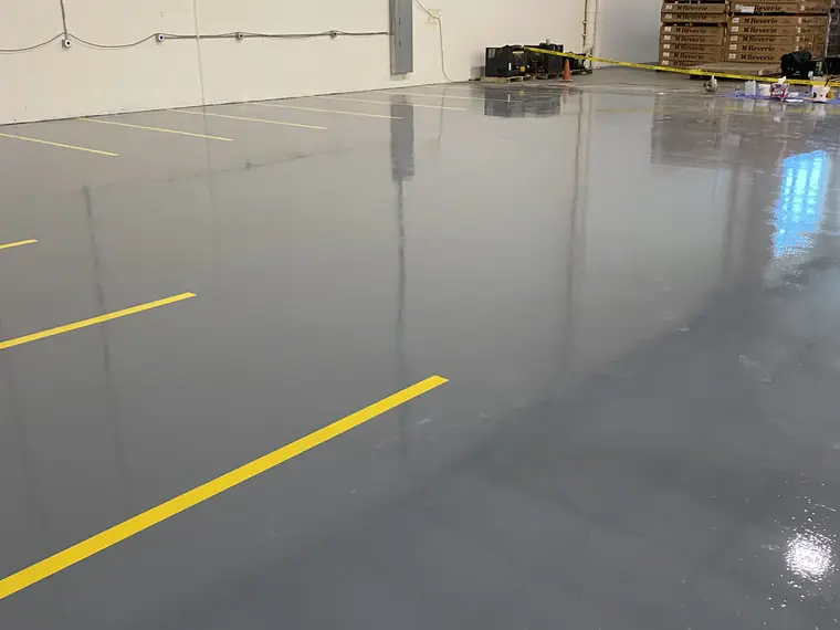 Gray epoxy floor with yellow lines leading toward stacked warehouse pallets