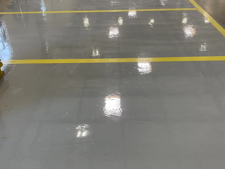 High-gloss gray epoxy warehouse floor reflecting the overhead lights between yellow lines