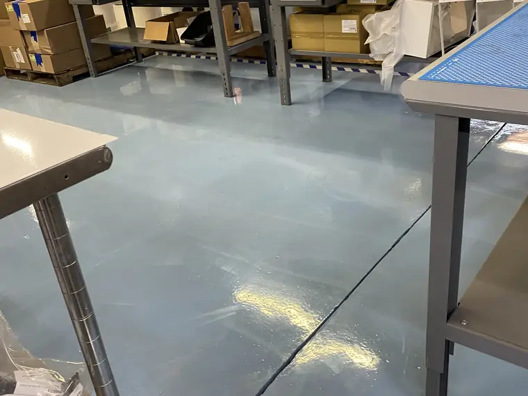 Pale blue epoxy floor beneath stainless workbenches in a production area