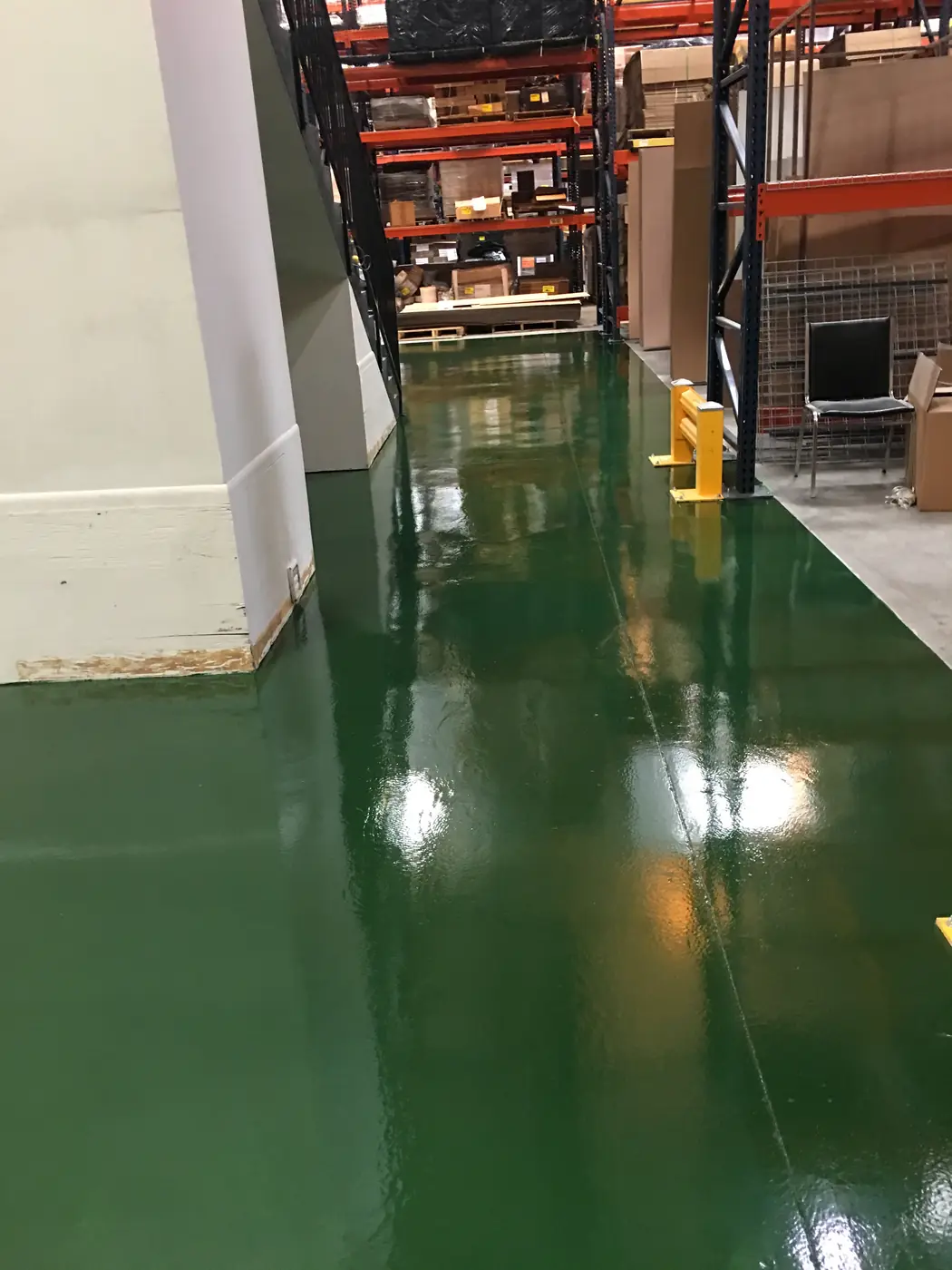 Green epoxy walkway passing warehouse racking and a yellow bollard