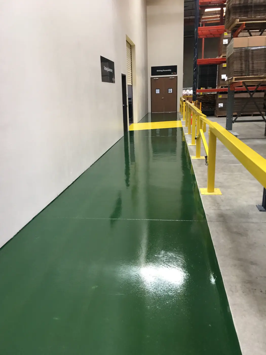 Green epoxy walkway running beside a yellow safety rail in a warehouse