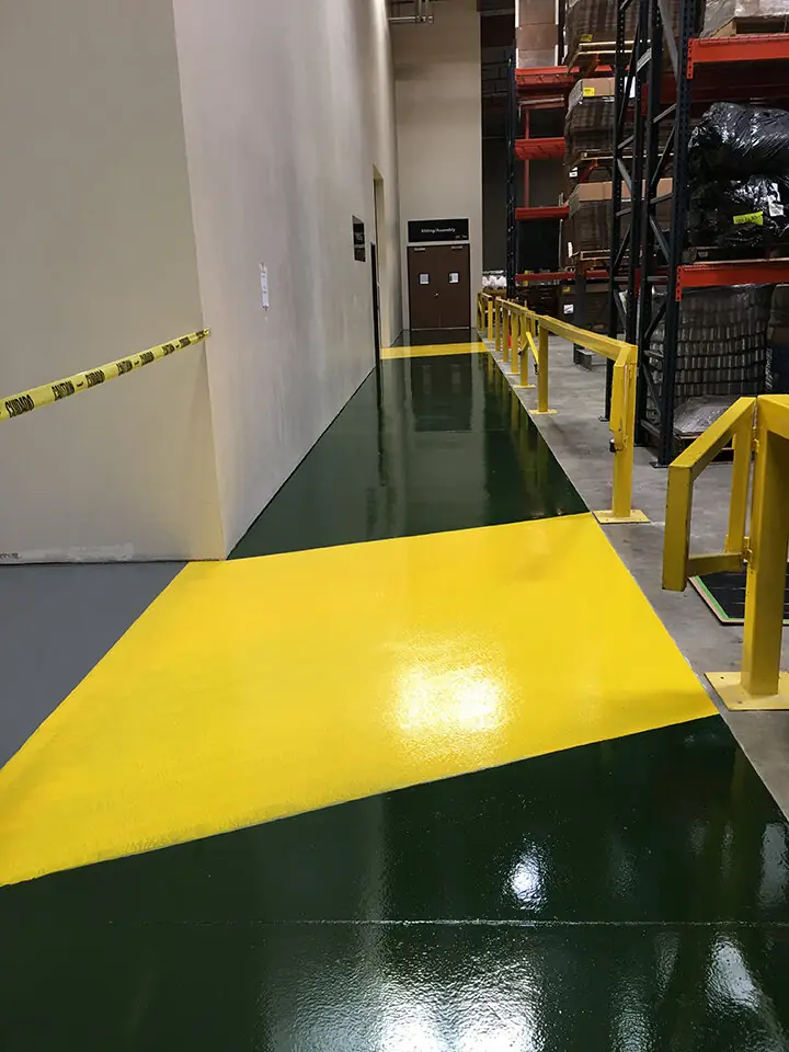 Green epoxy floor with a yellow safety stripe along its edge