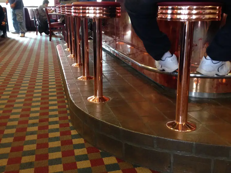 Diner counter with copper stools standing on a red and gold checcurboard floor overlay