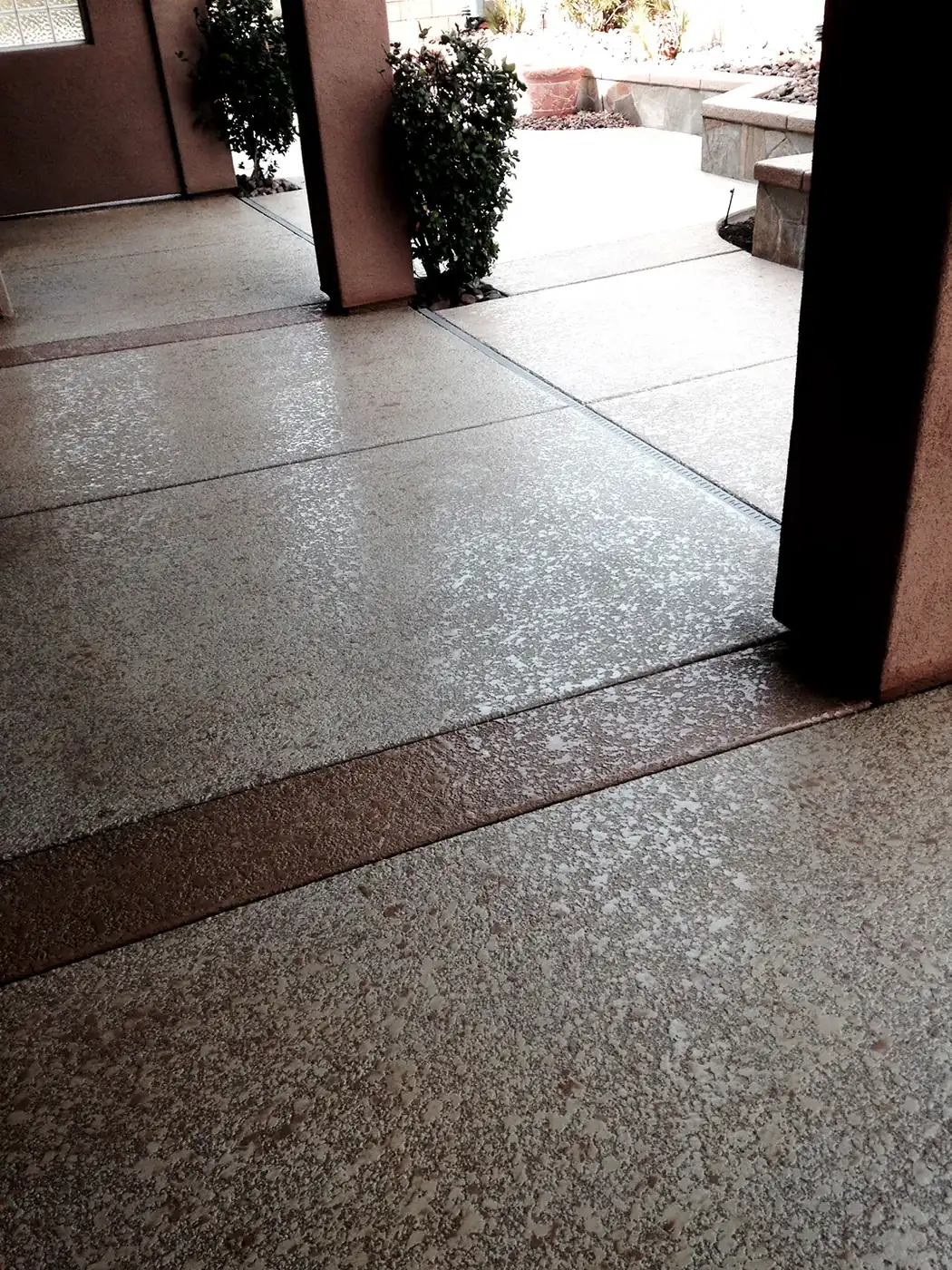 Speckled overlay patio beside a stucco column and hedge