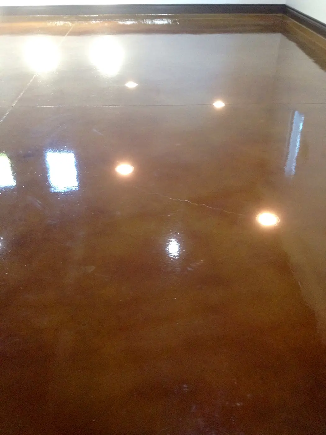 Glossy brown stained concrete floor reflecting ceiling downlights