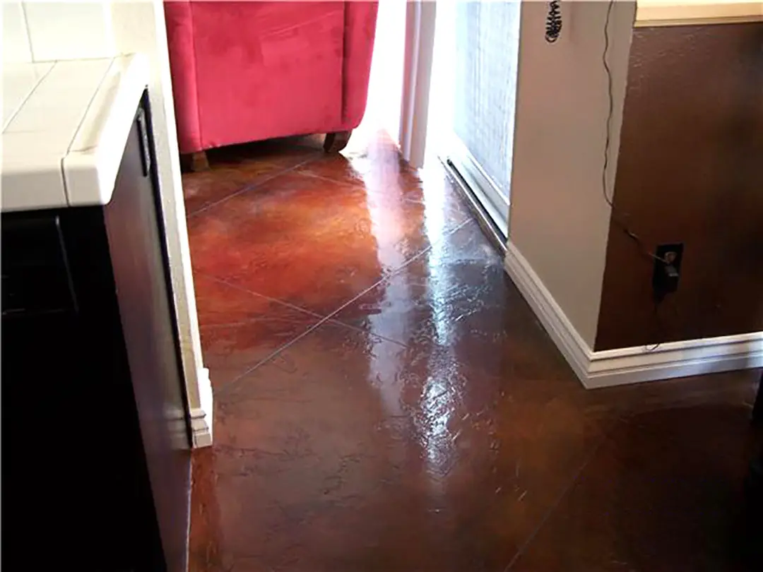 Red-brown stained concrete floor in a kitchen beside a red armchair