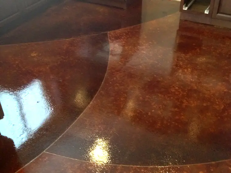 Dark red stained concrete floor curving into a kitchen