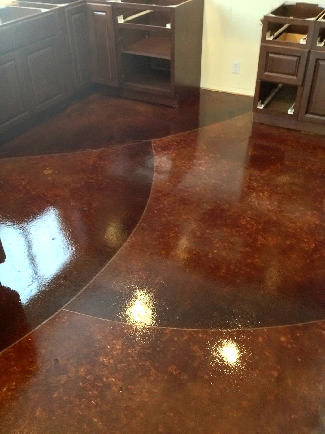 Dark red stained concrete floor curving into a kitchen