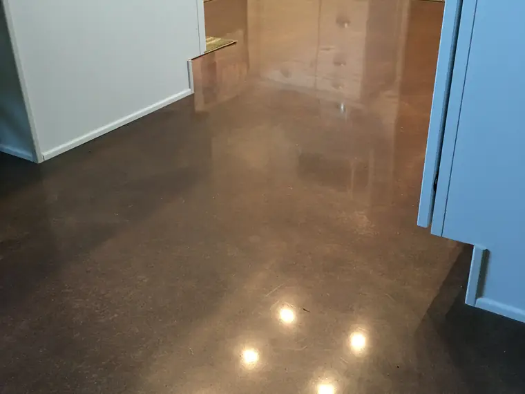 Brown stained and polished concrete floor in a kitchen with pale cabinetry