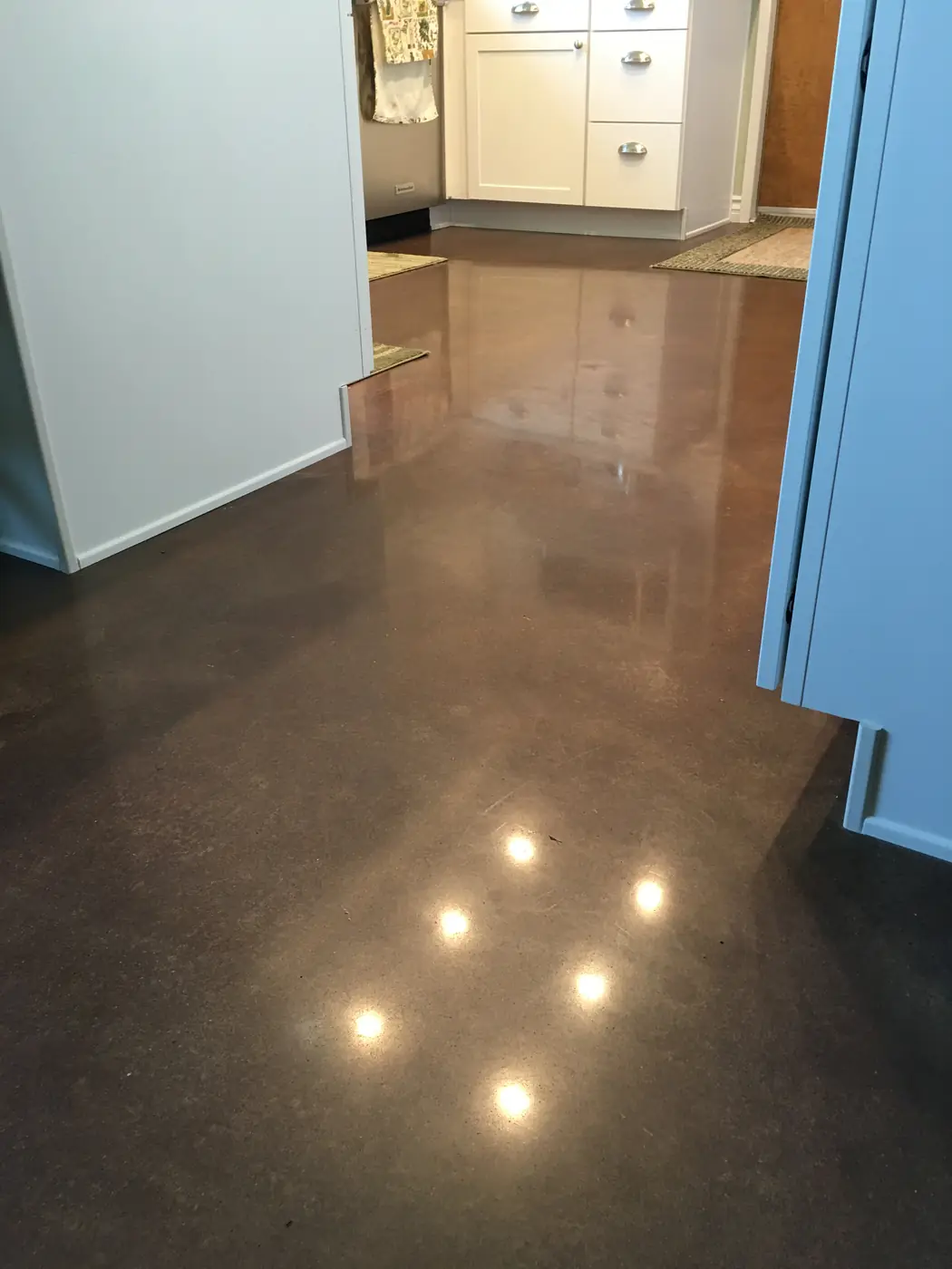 Brown stained and polished concrete floor in a kitchen with pale cabinetry