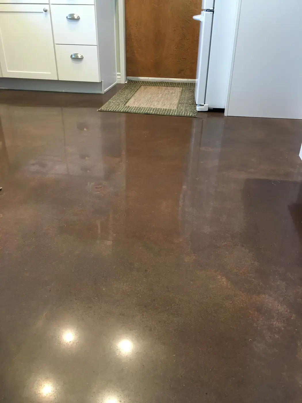 Brown polished concrete kitchen floor with rugs and appliances