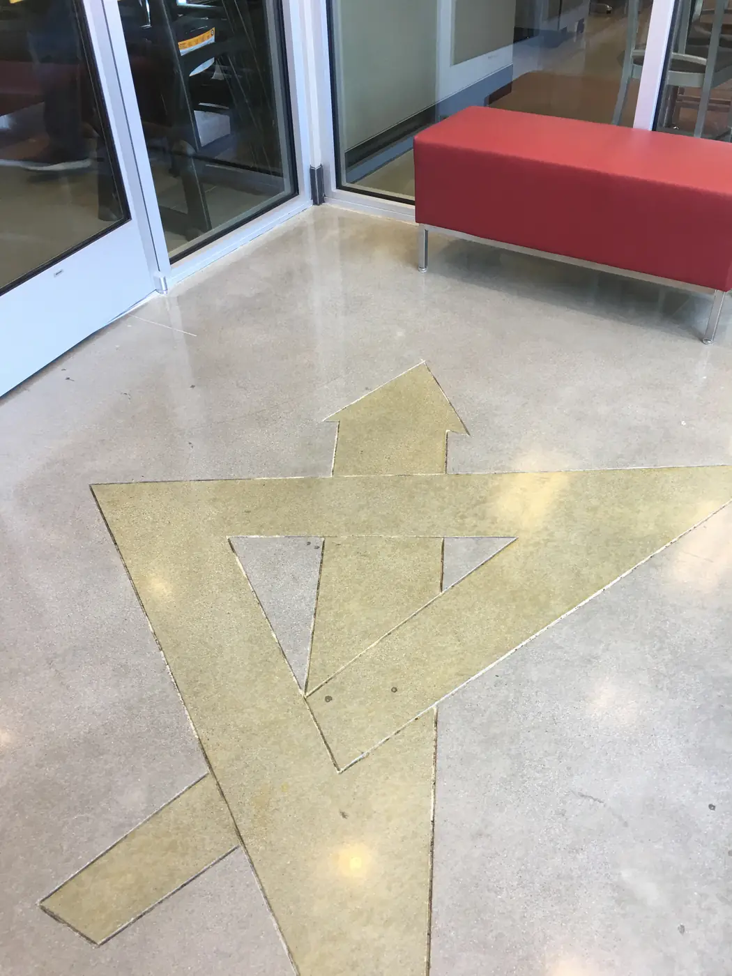 Gold stained arrow and triangle graphic in a polished floor beside a red bench
