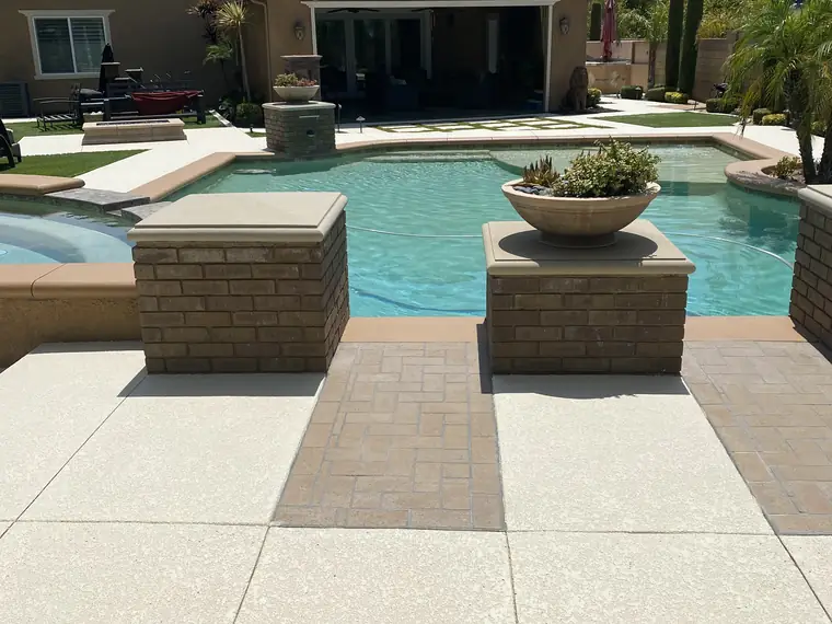 Wide backyard pool with a cream deck and brick planter walls behind a family home
